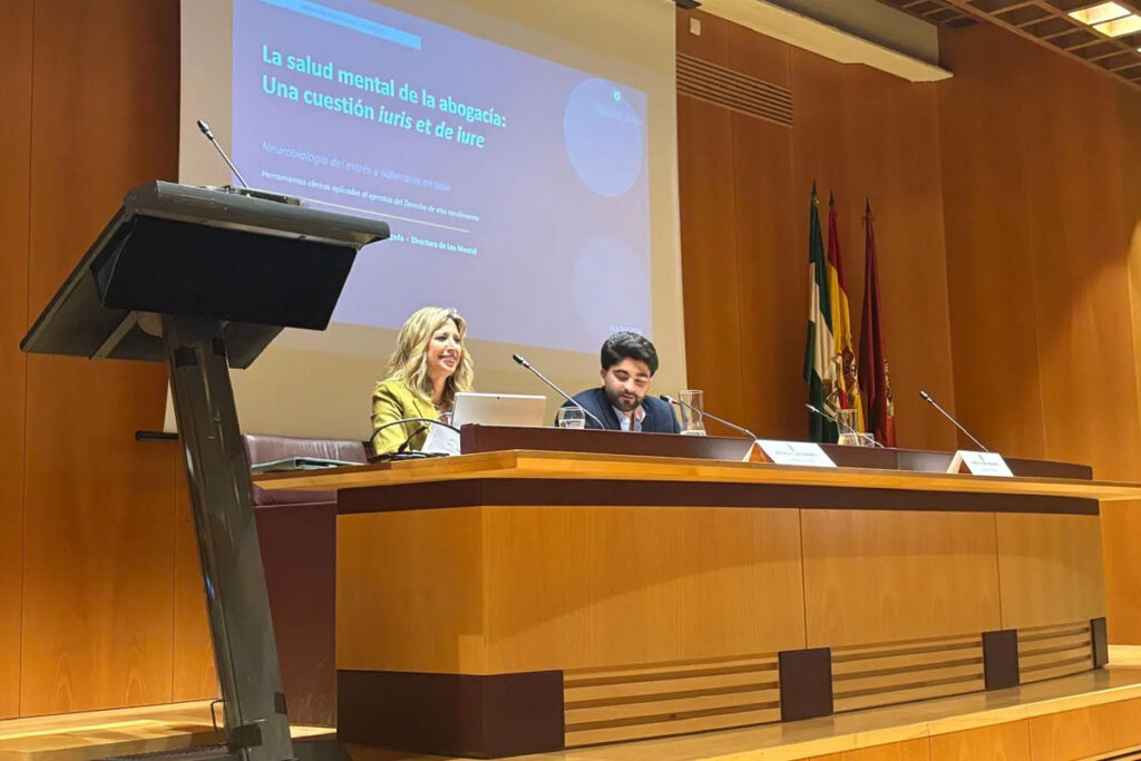 Patricia Tudó en la mesa de una jornada institucional, con su ponencia «La salud mental de la abogacía: una cuestión iuris et de iure» proyectada al fondo